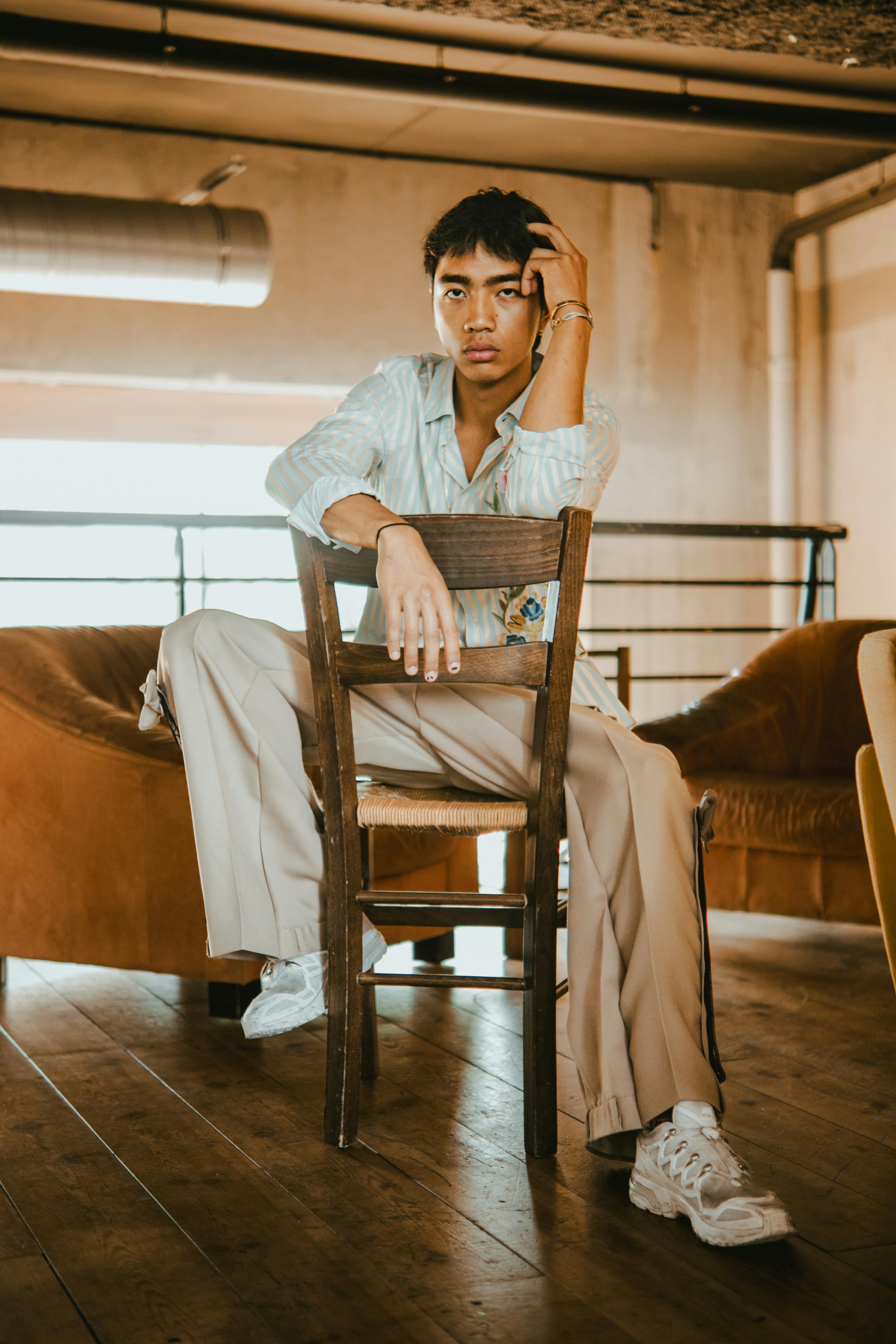 Man in neutral colors sitting backwards on a wooden chair in neutral colored room