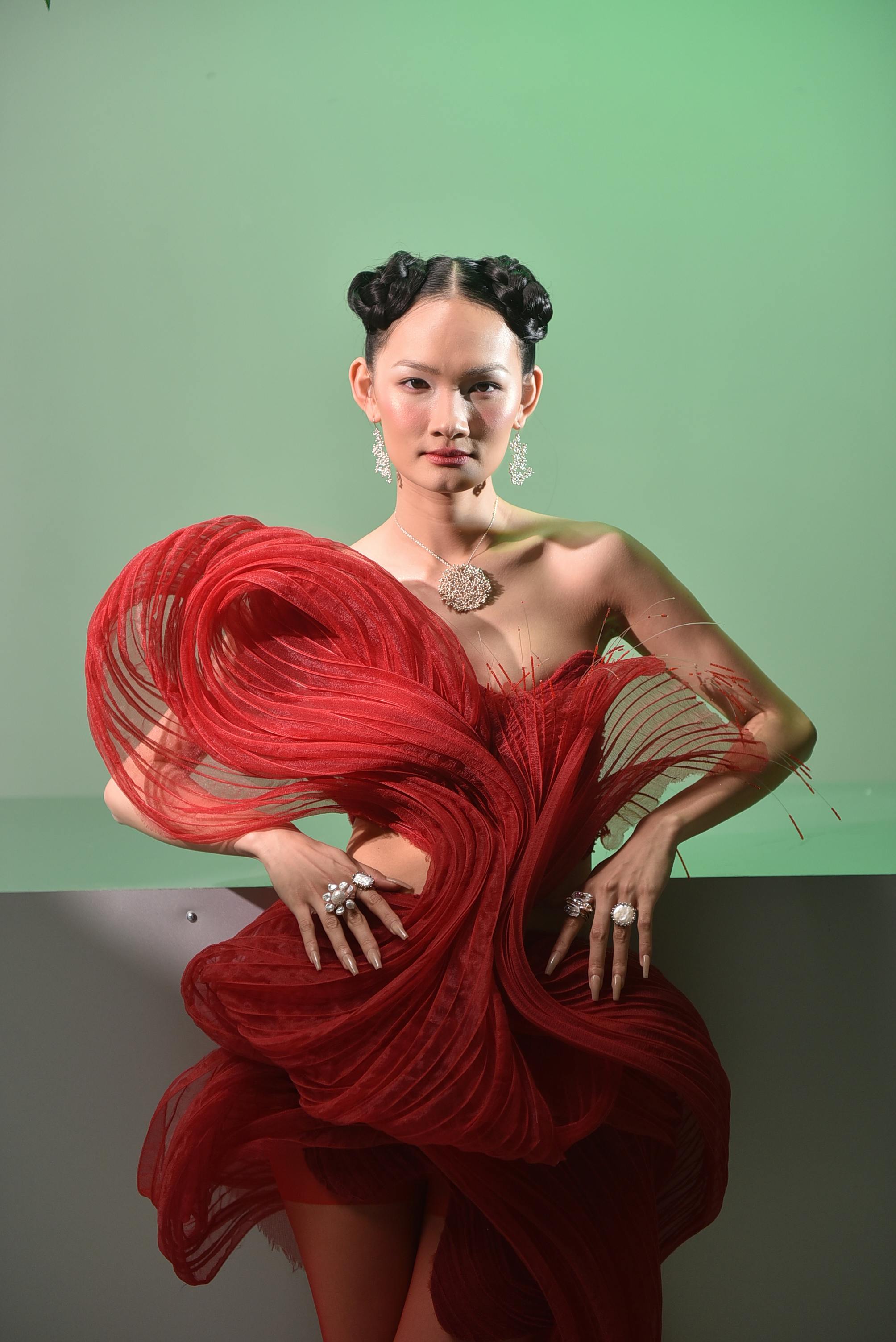Editorial image of a girl in a unique red dress structured with curves and and two braided buns in front of a light green background